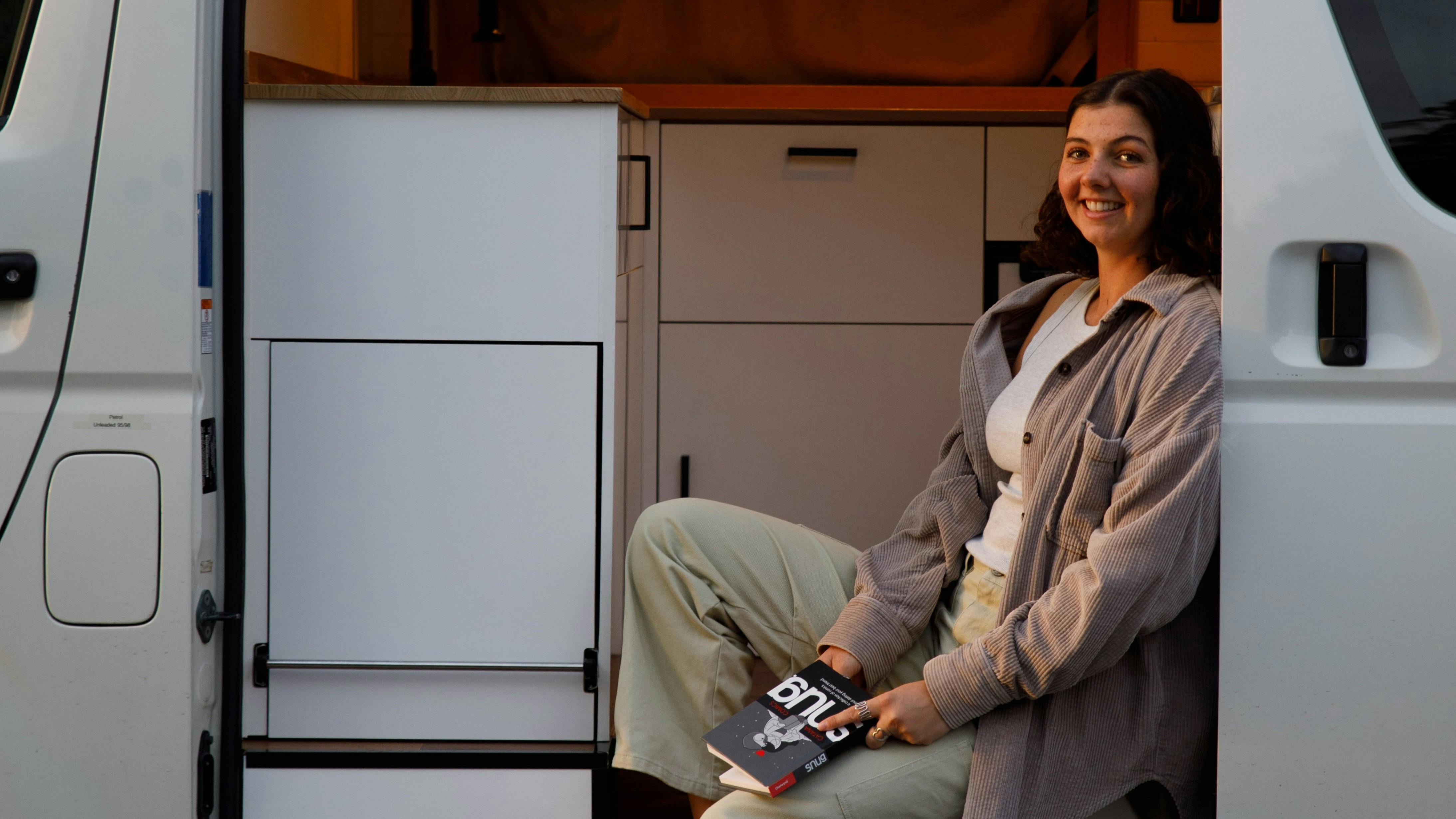 Relaxing inside campervan with a book at sunset on a Tasmanian road trip.