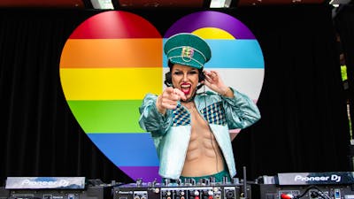 Dj Sexy Galexy boi drag performer and DJ playing music at Fair day Large Rainbow Heart in the backgr