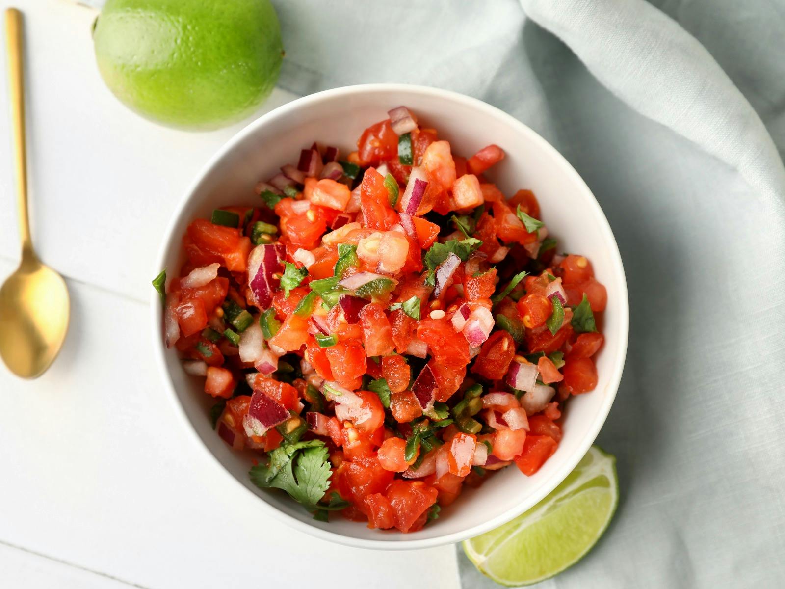 Bowl of vibrant red tomato salsa on table with lime and lime wedge for garnish
