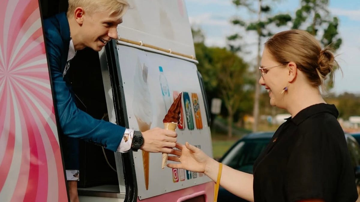 A young man in formal attire serves a choc top soft serve cone from the World of Swirls van. A young man in formal attire serves a choc top soft serve cone from the World of Swirls van.