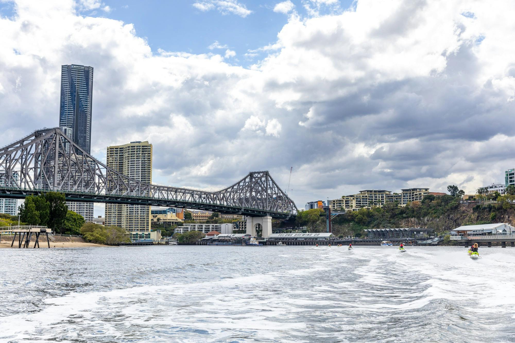 Group of people riding jet skis on Brisbane River with Story Bridge in background.