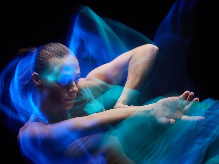 A dancer bathed in blue light holds her hand out towards the camera.
