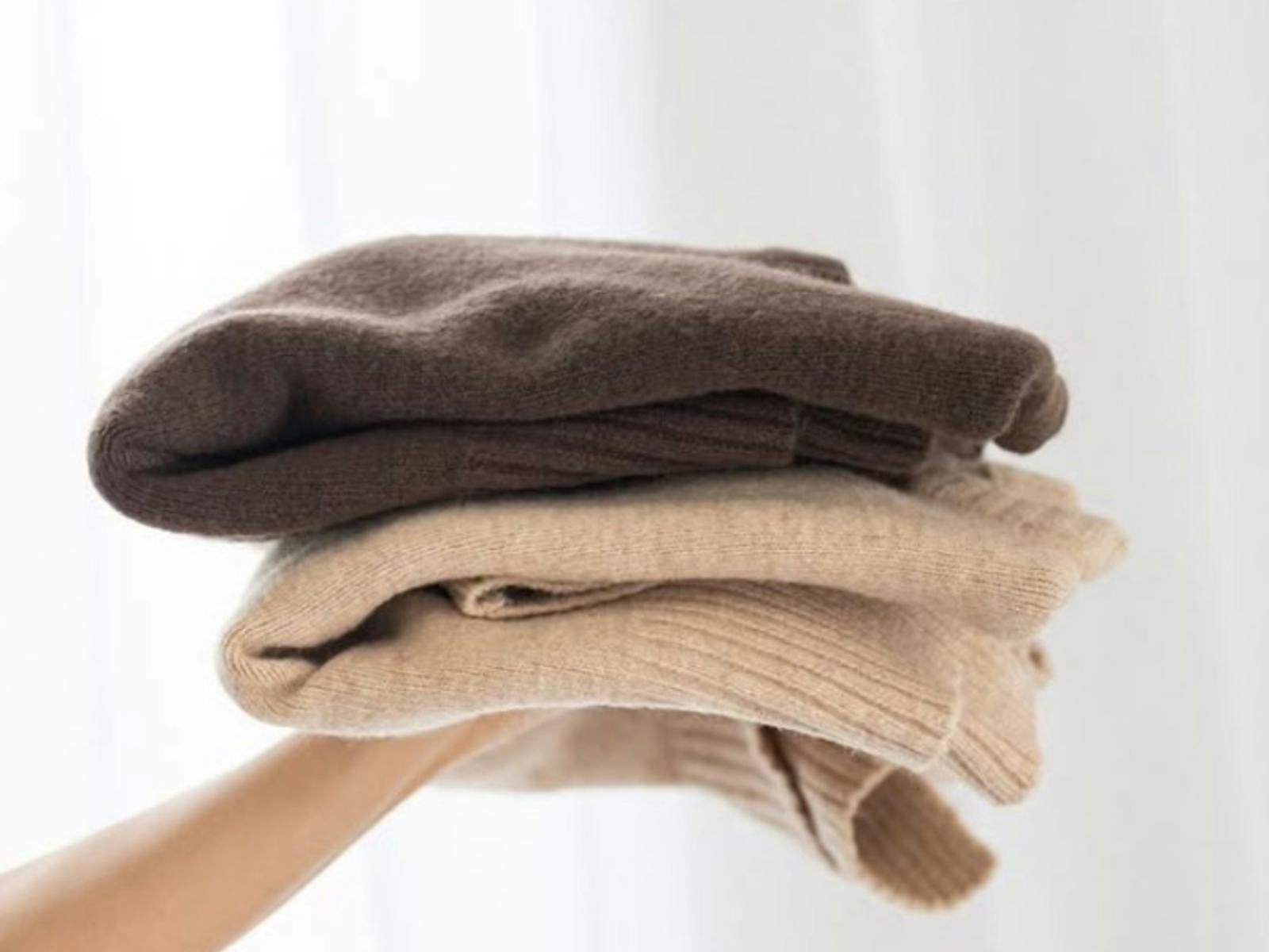 A hand holding up two knitted jumpers
