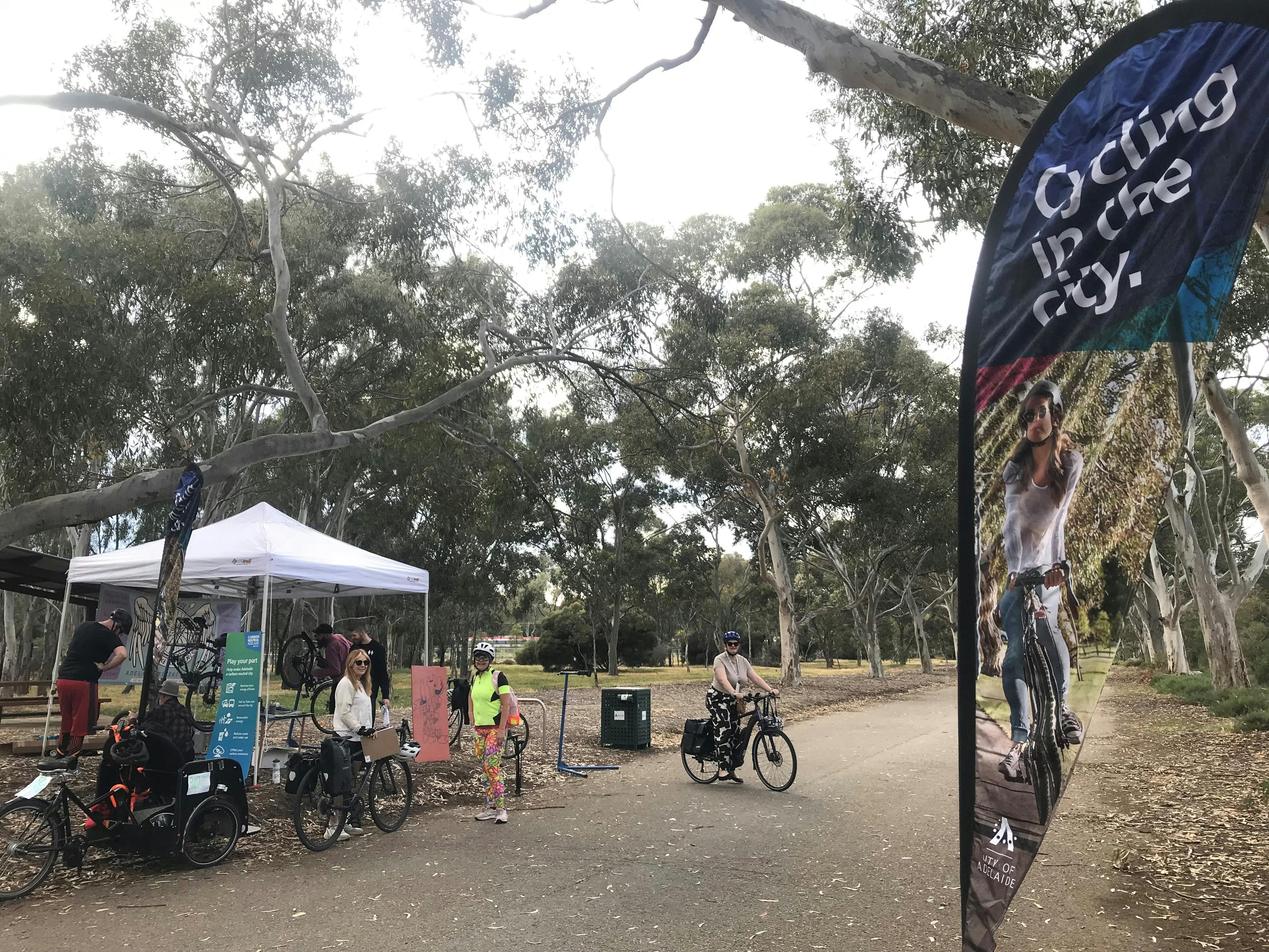 People who have been cycling are chatting as their bikes are tuned-up under a marquee in Park Lands.