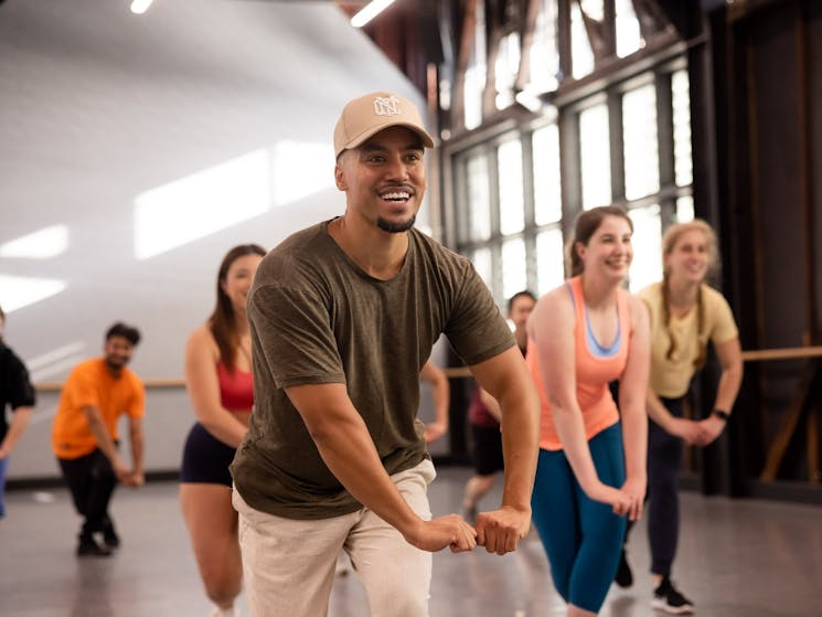 Man wearing a green shirt and beige hat is posing in a Studio hip-hop class with other attendees