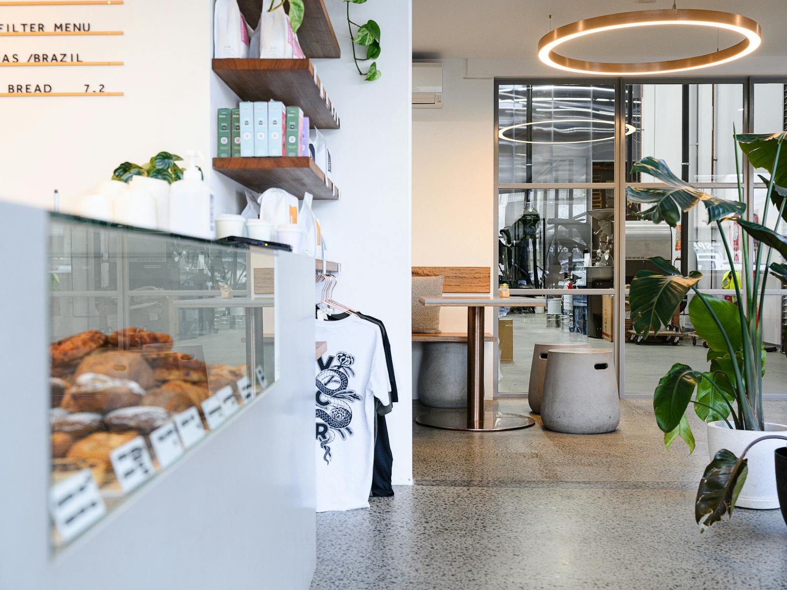 A light, modern cafe space with large windows between a seating area and the roastery space.