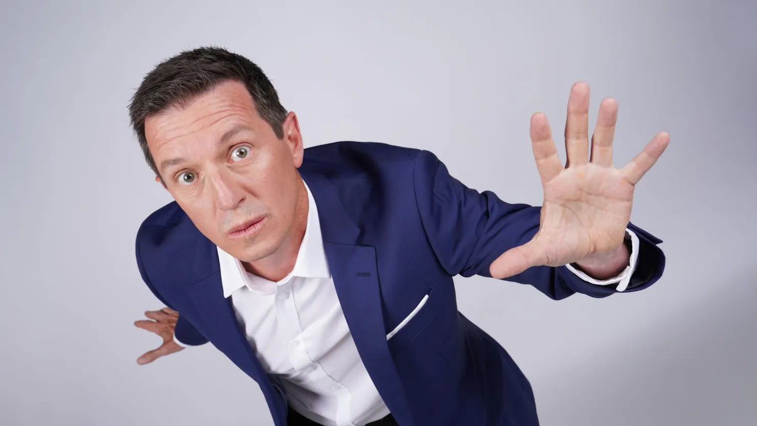 Rove in a blue suit jacket and white shirt looking up with left hand up