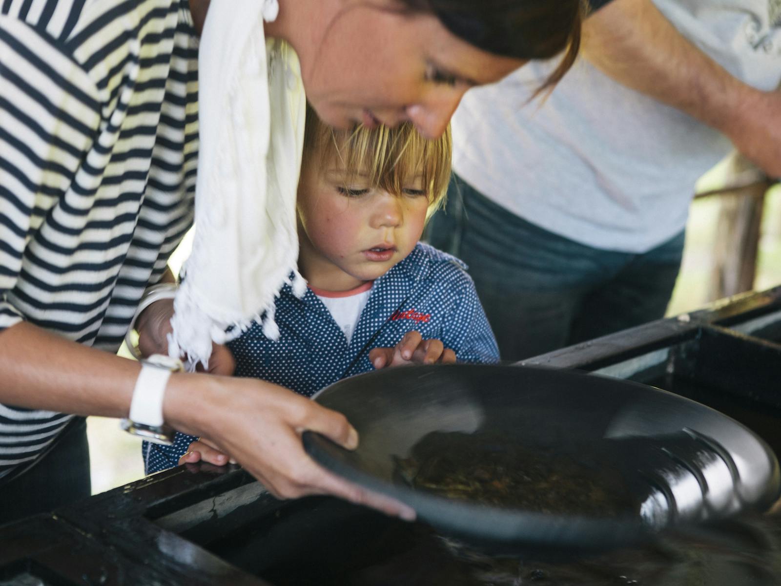 A woman and child gaze into a panning tray searching for gold