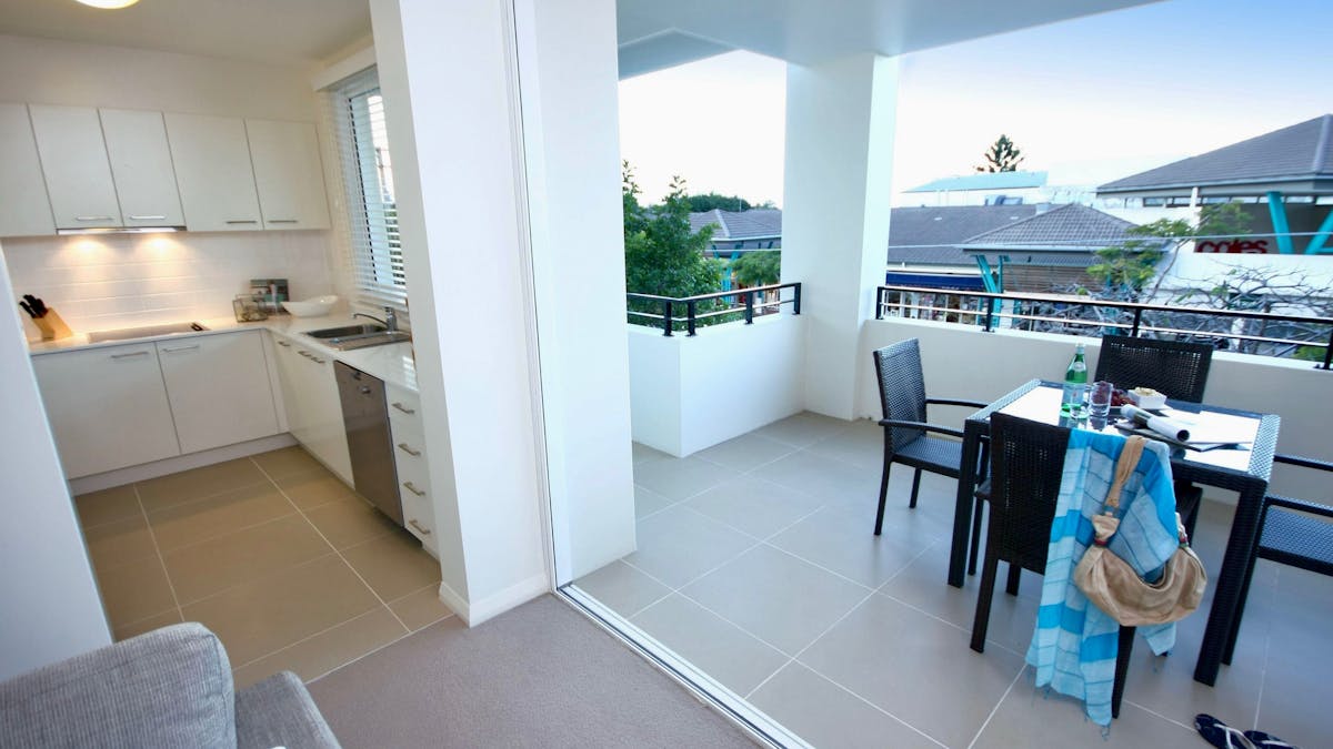 Open-plan kitchen with dishwasher alongside a covered balcony with outdoor dining table overlooking