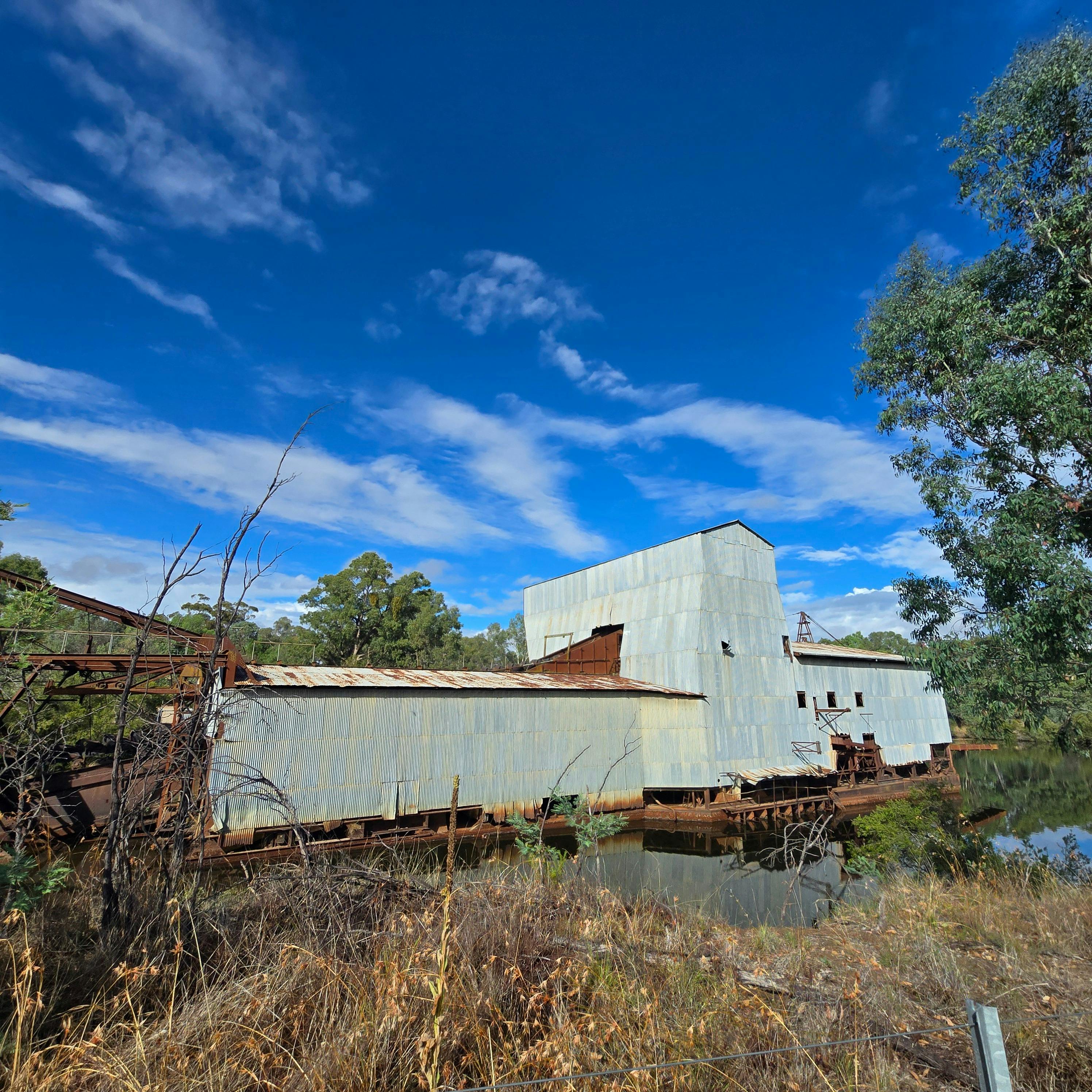 A photograph of the Eldorado Dredge, a massive, rusting gold mining dredge, sits partially submerged