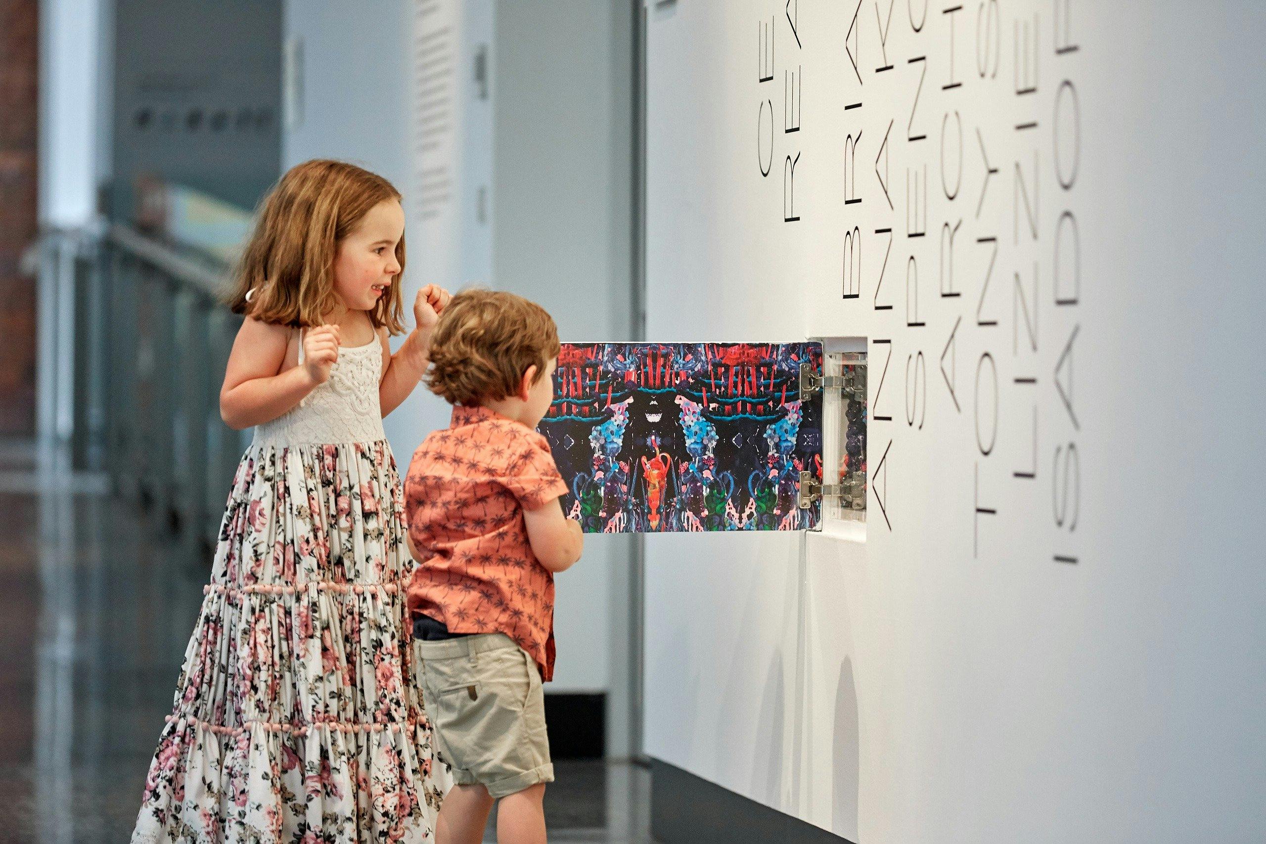 Two children open a cupboard with an art installation inside