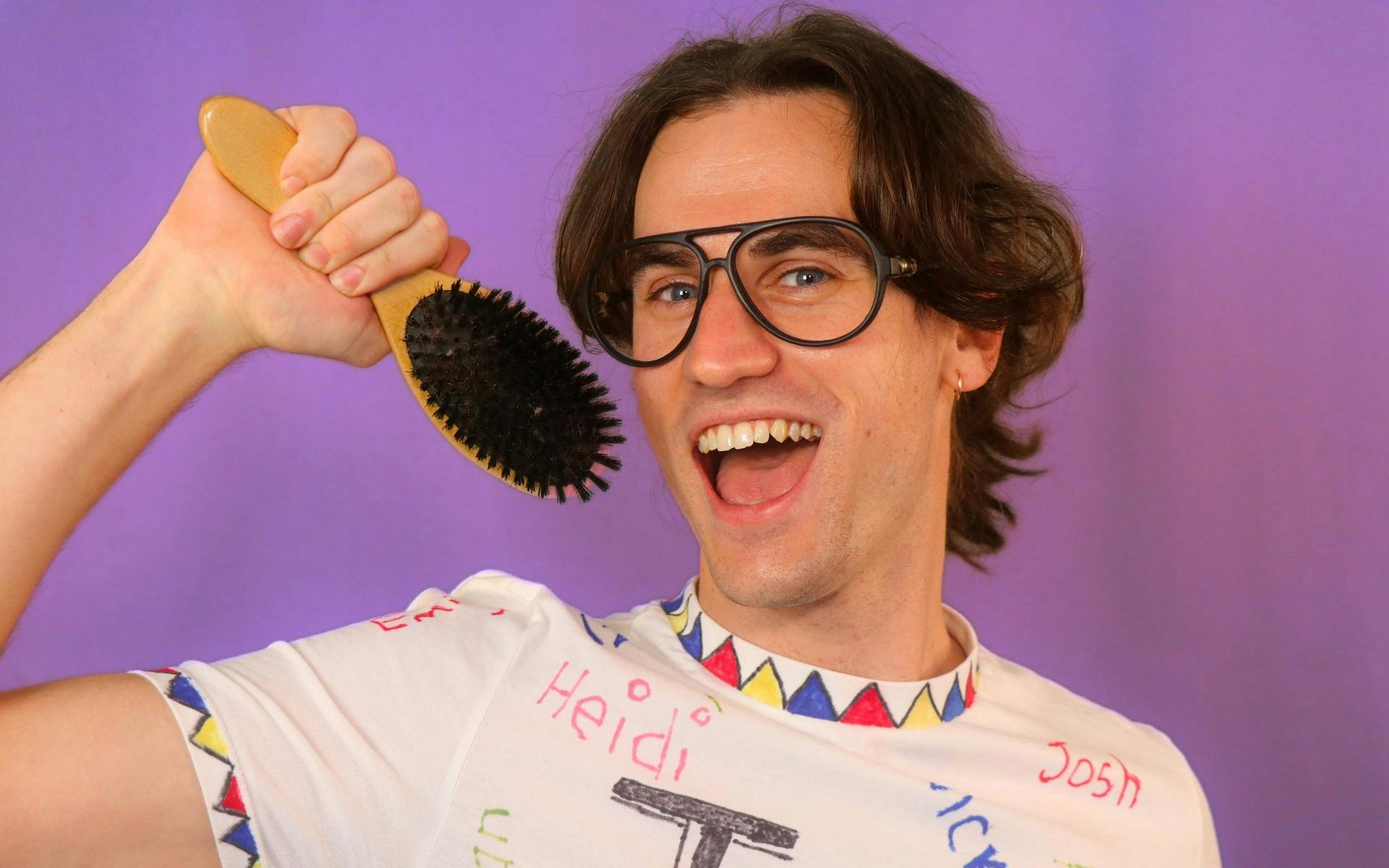 Taylor Swift fan in fan made tshirt smiles widley holding a hairbrush like a microphone.