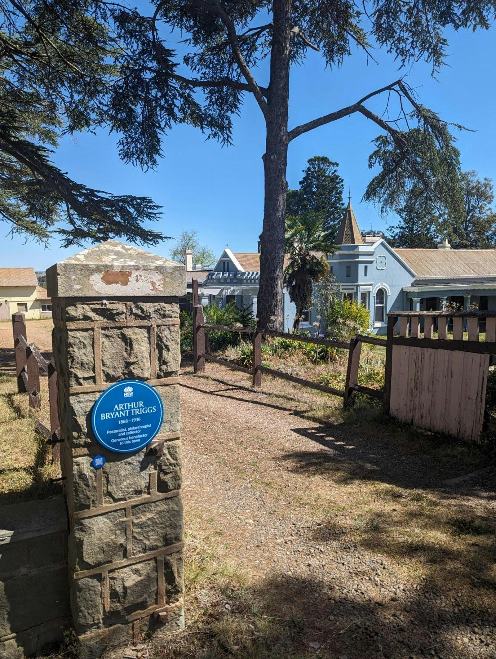 Blue plaque and QR code on stone fence plinth next to driveway and houses in the background