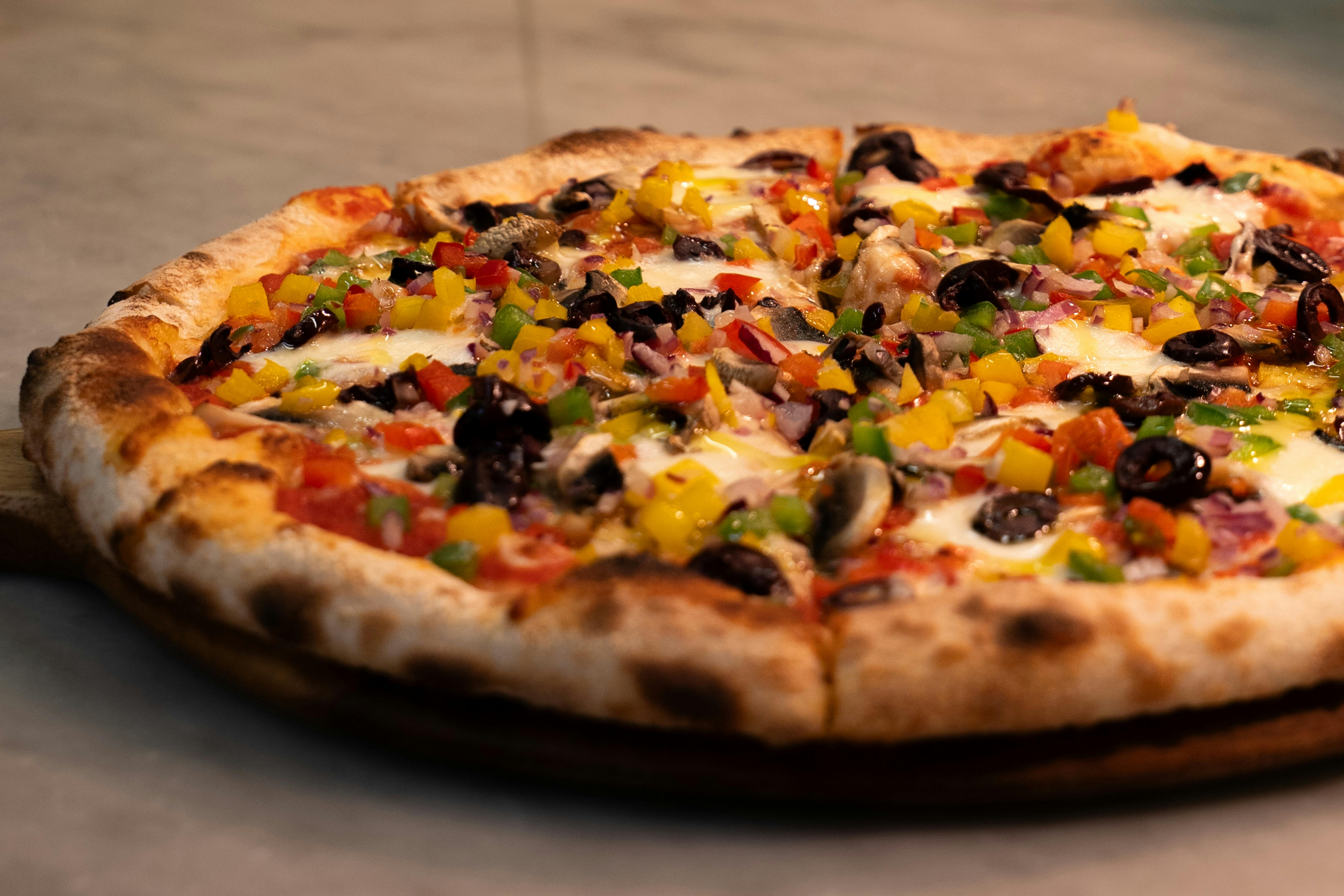 A loaded pizza with olives and peppers, fresh on the pass.