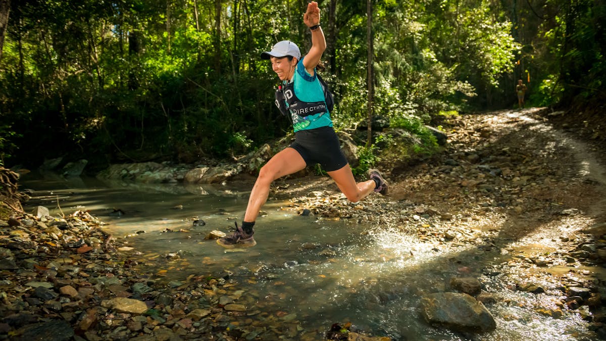 A runner leaping over a creek at the bottom of Hell Hole Break
