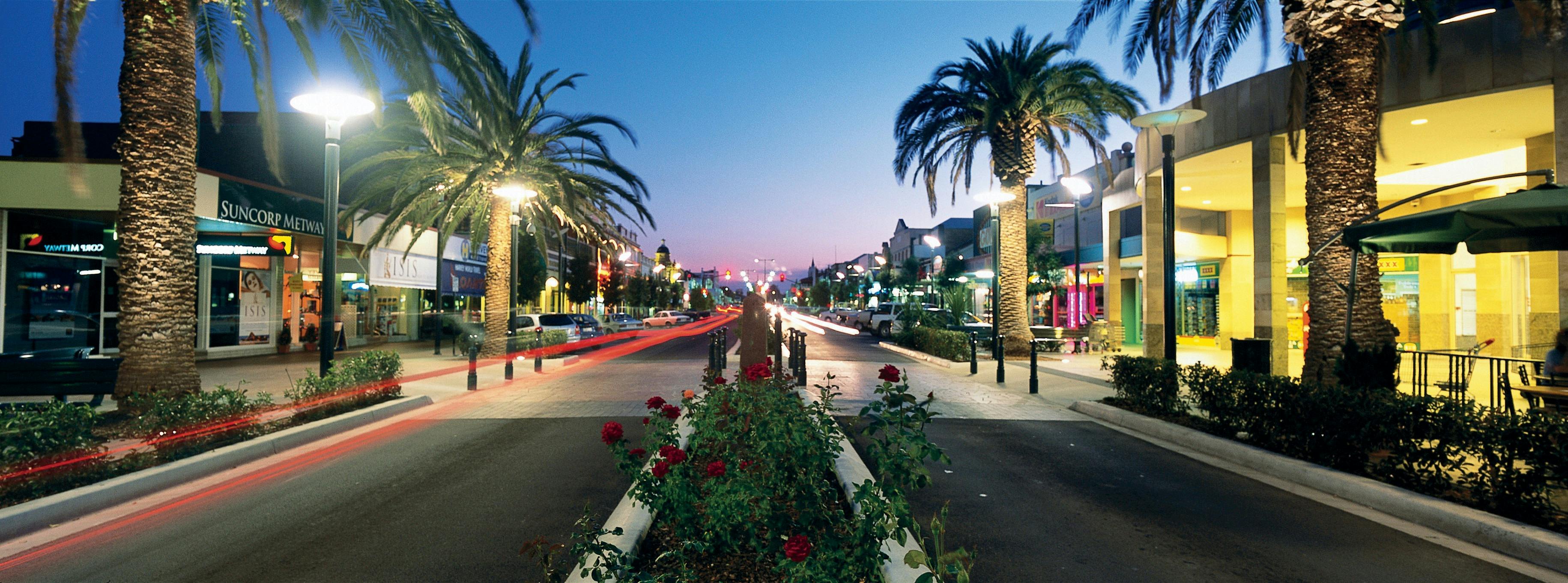 Photo shows part of Warwick's main street at dusk, with rose beds in centre, palm trees at sides