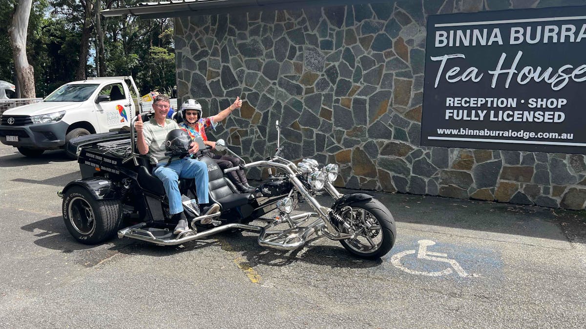 Image shows two passengers on the back of the trike in front of the Binna Burra Tea house.