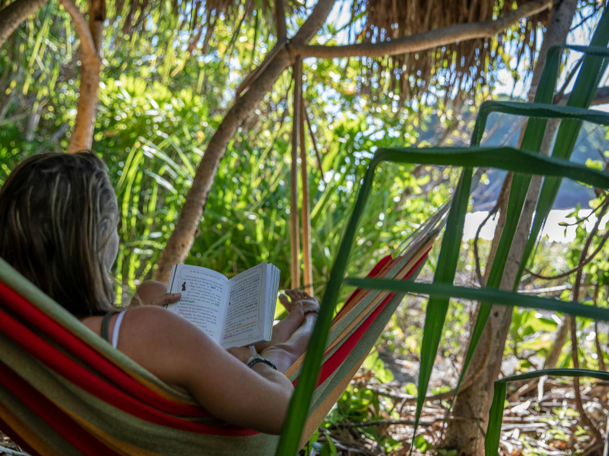 A caucasian woman reads in a hammock on a tropical island
