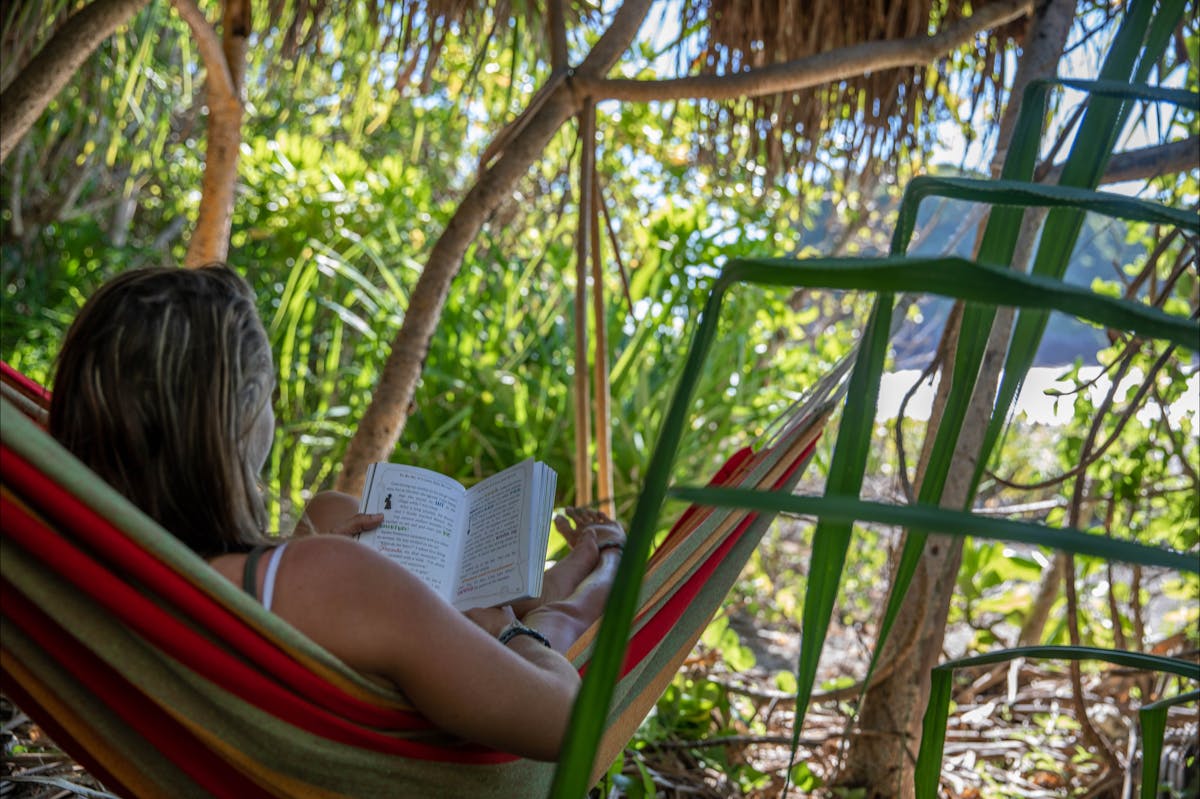 A caucasian woman reads in a hammock on a tropical island