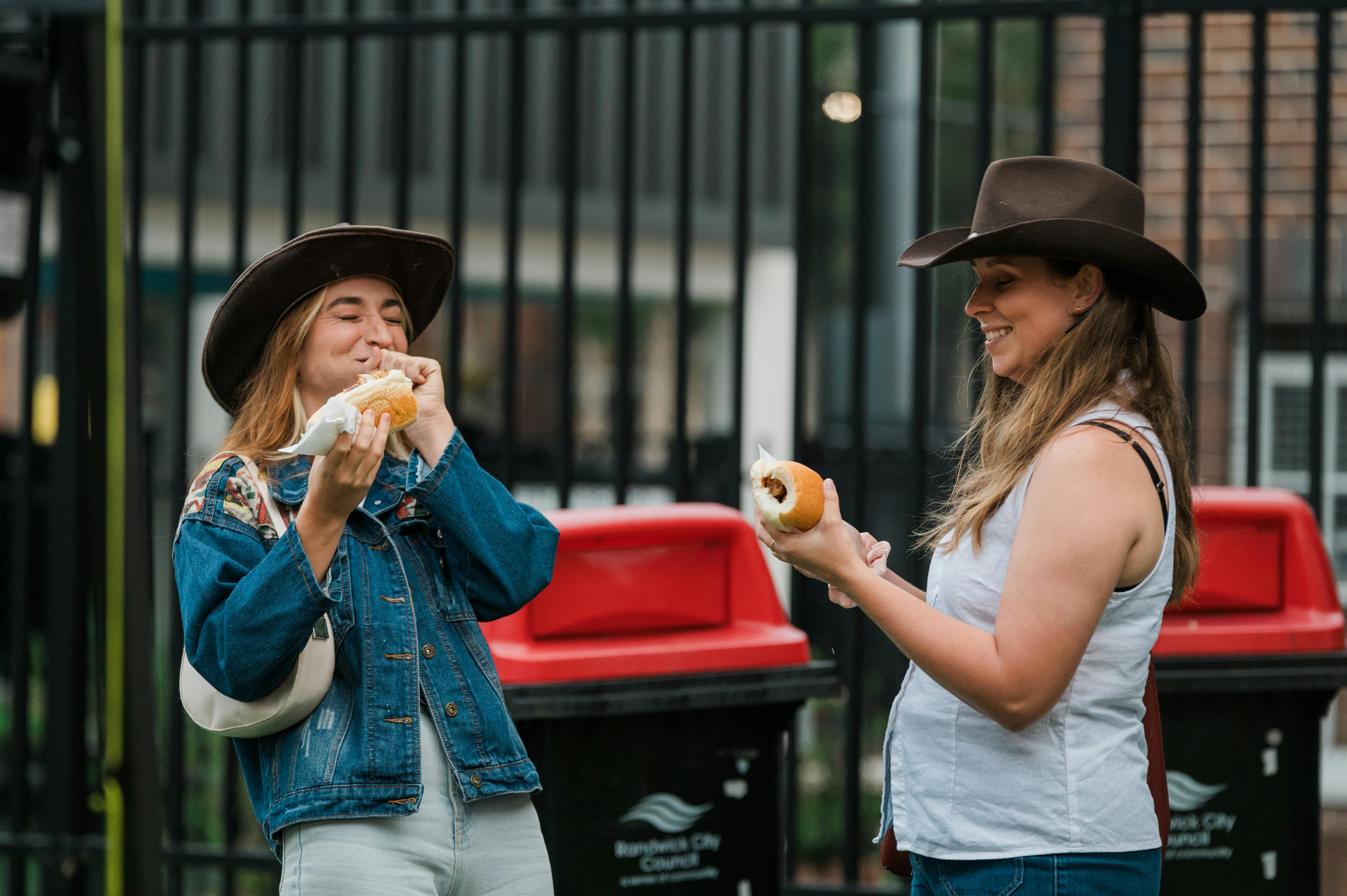 Two people in cowboy hats  eat sausages