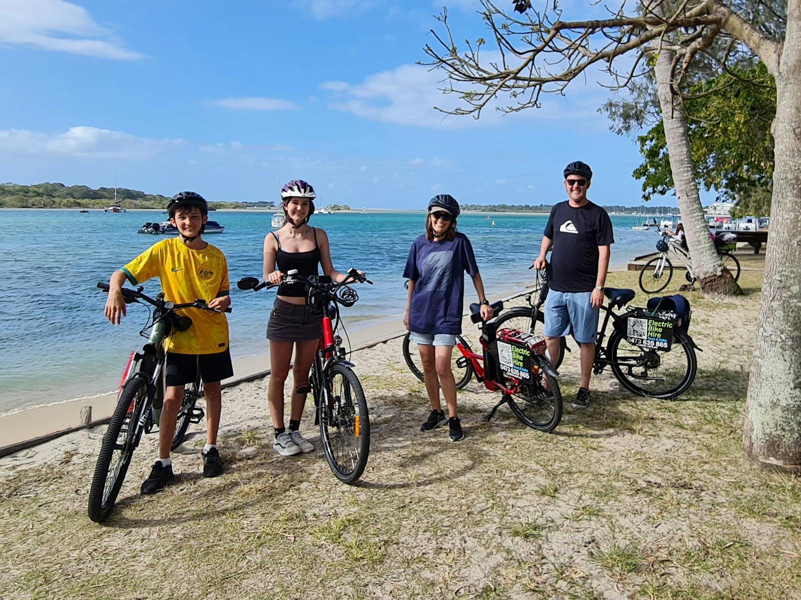 Family of four resting beside Noosa River, bikes parked, during a scenic e-bike tour Family of four resting beside Noosa River, bikes parked, during a scenic e-bike tour