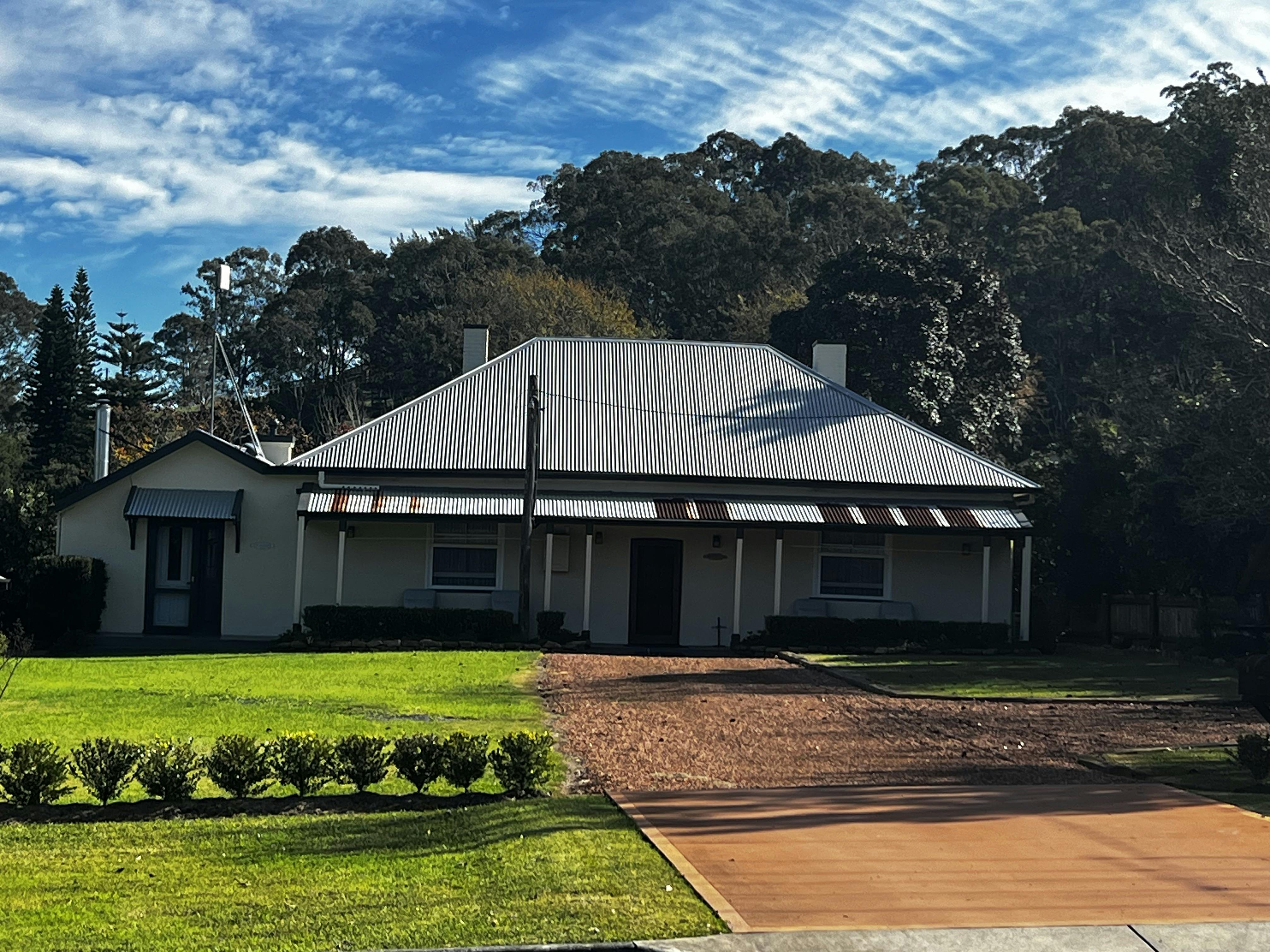 Single-storey heritage cottage with corrugated iron roof and wraparound verandah, set on a lawn.