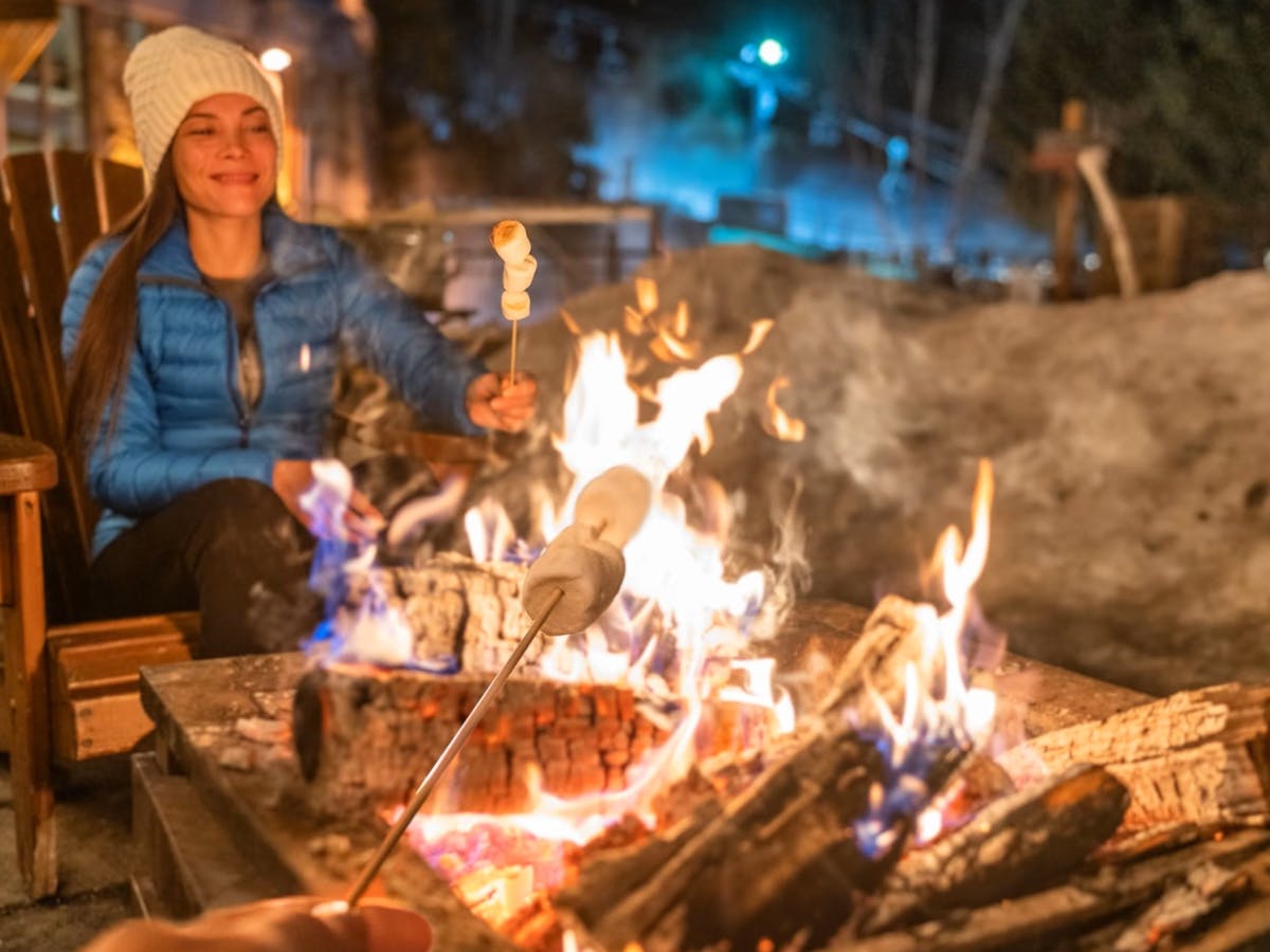 Sitting around firepit toasting marshmallows with snow in background