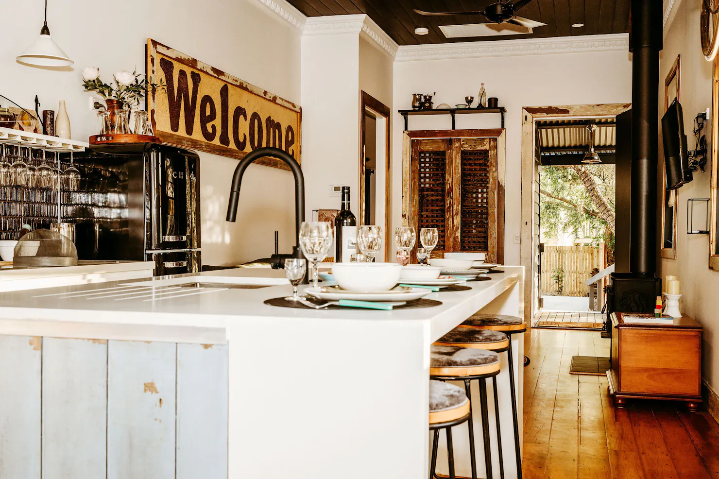 Kitchen bench features with ecclectic crockery and glassware. Welcome sign in dstance as artwork.