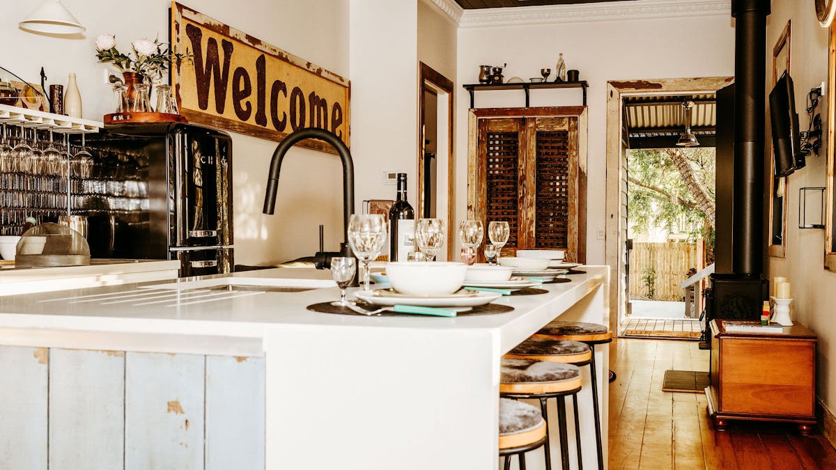Kitchen bench features with ecclectic crockery and glassware. Welcome sign in dstance as artwork.