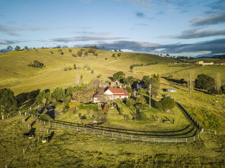 Aerial view of red roofed farmhouse with rolling green hills behind and blue skies