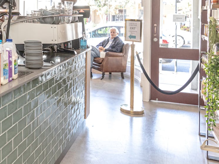 Green tiled bar with display shelves, plants, waitress preparing cakes