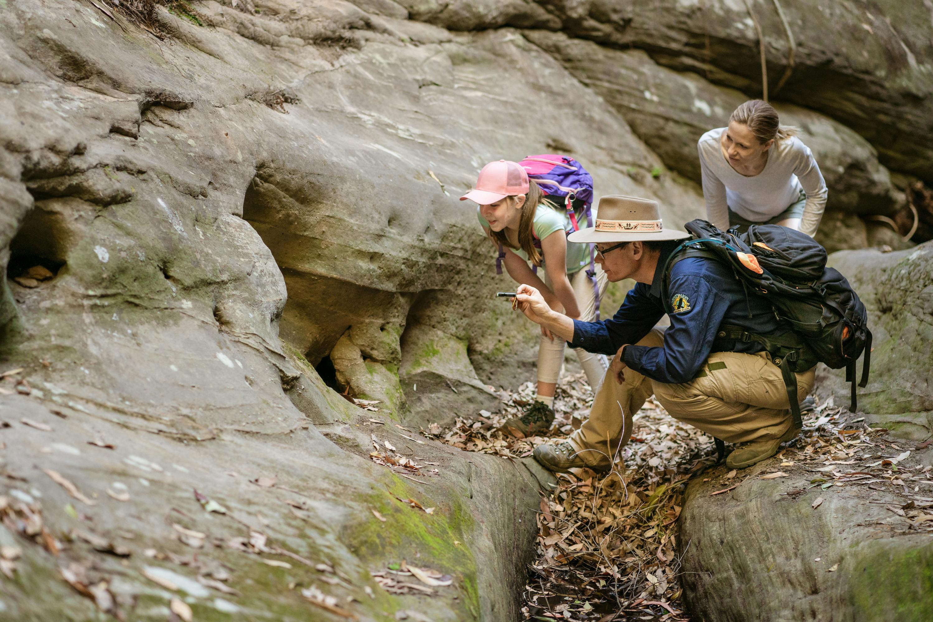 A tour guide shines his torch into the crevice of a sandstone cliff for his guests, Carnarvon Gorge.
