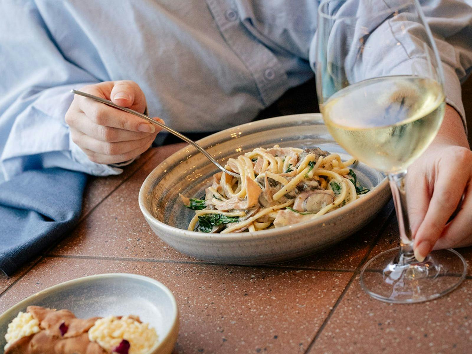 Pasta in a bowl being twirled on a fork with a glass of white wine
