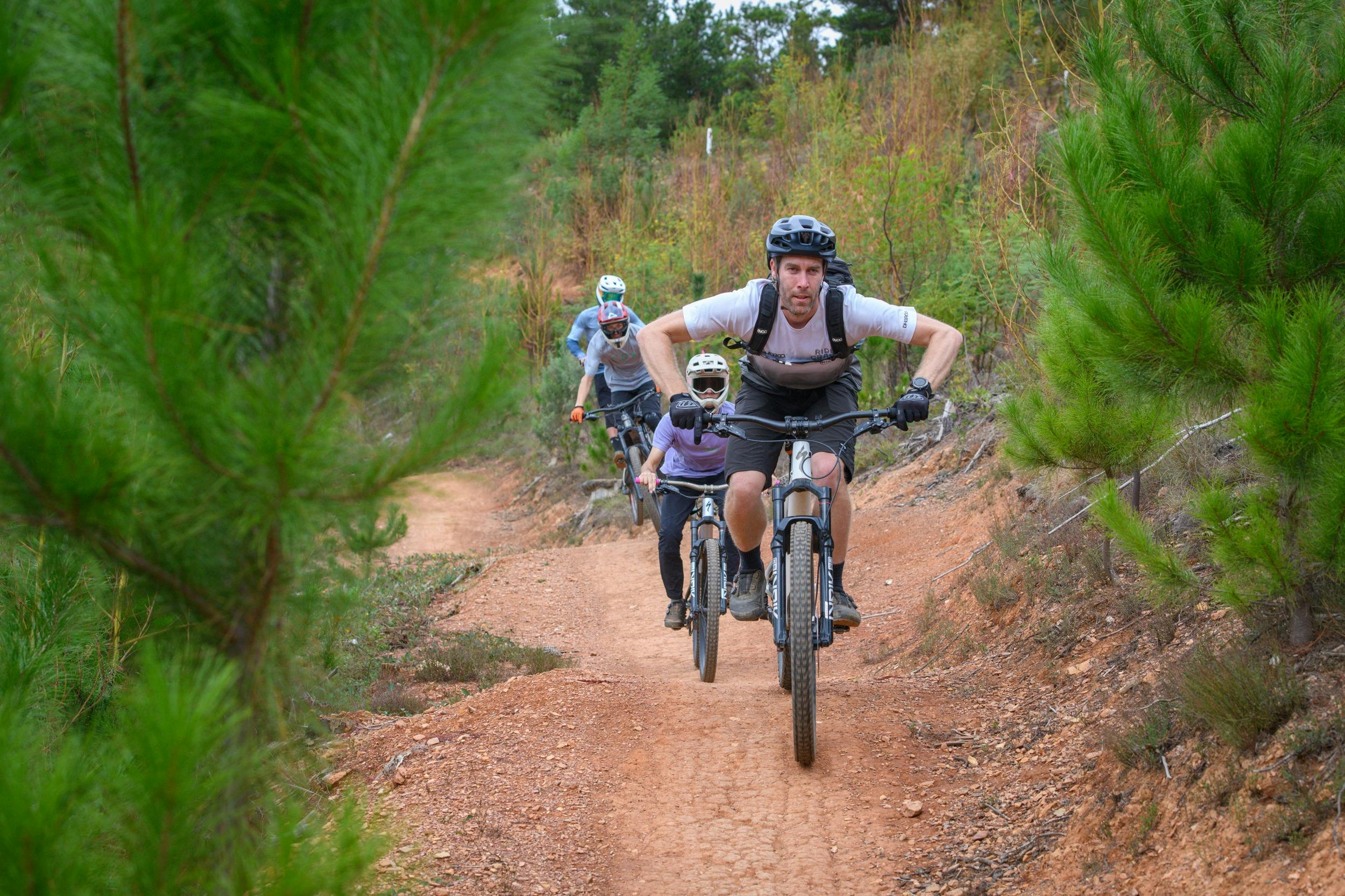 A group of riders on bikes jump follow a coach along a trail.