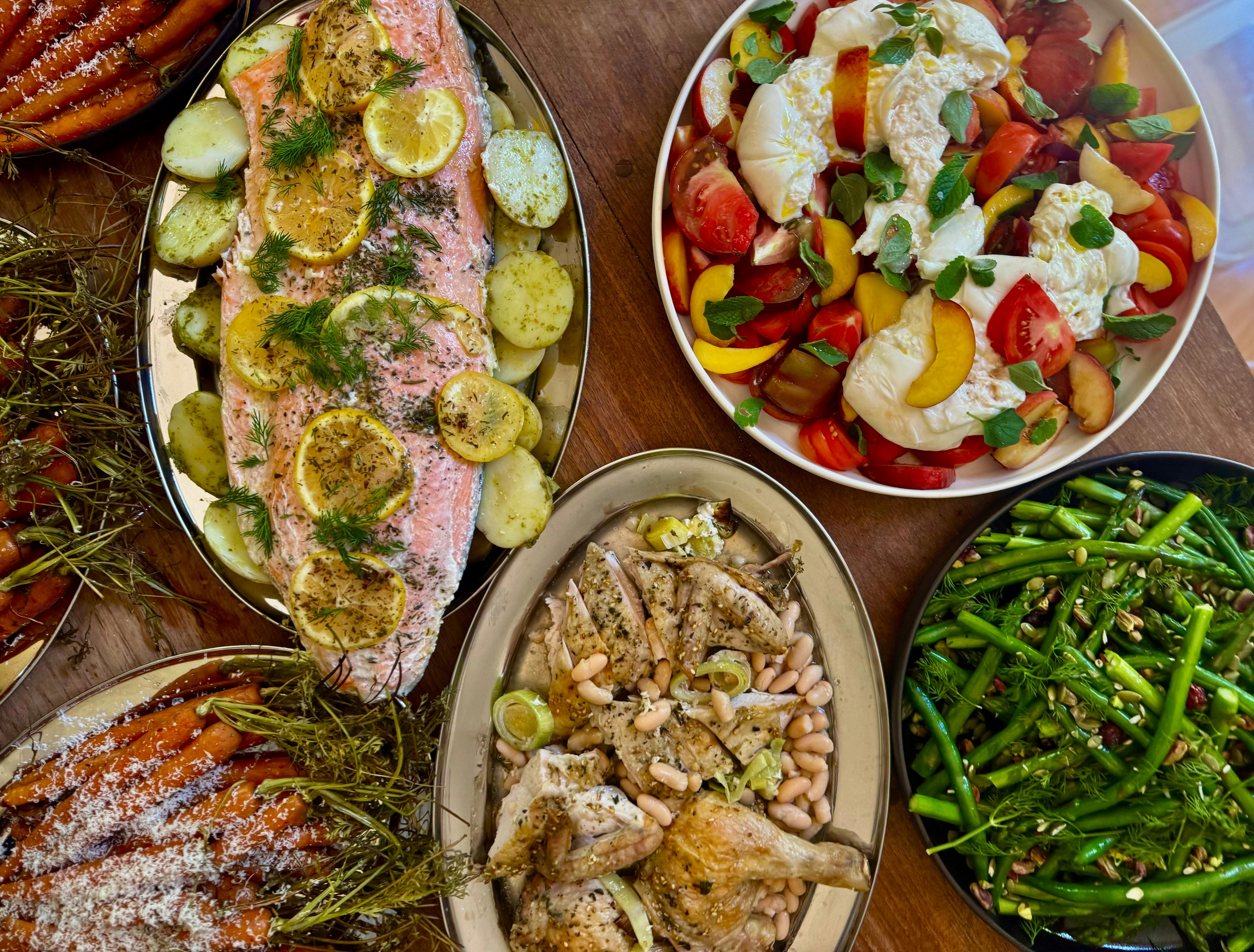 A table filled with platters of food including grilled salmon, roast chicken and salads
