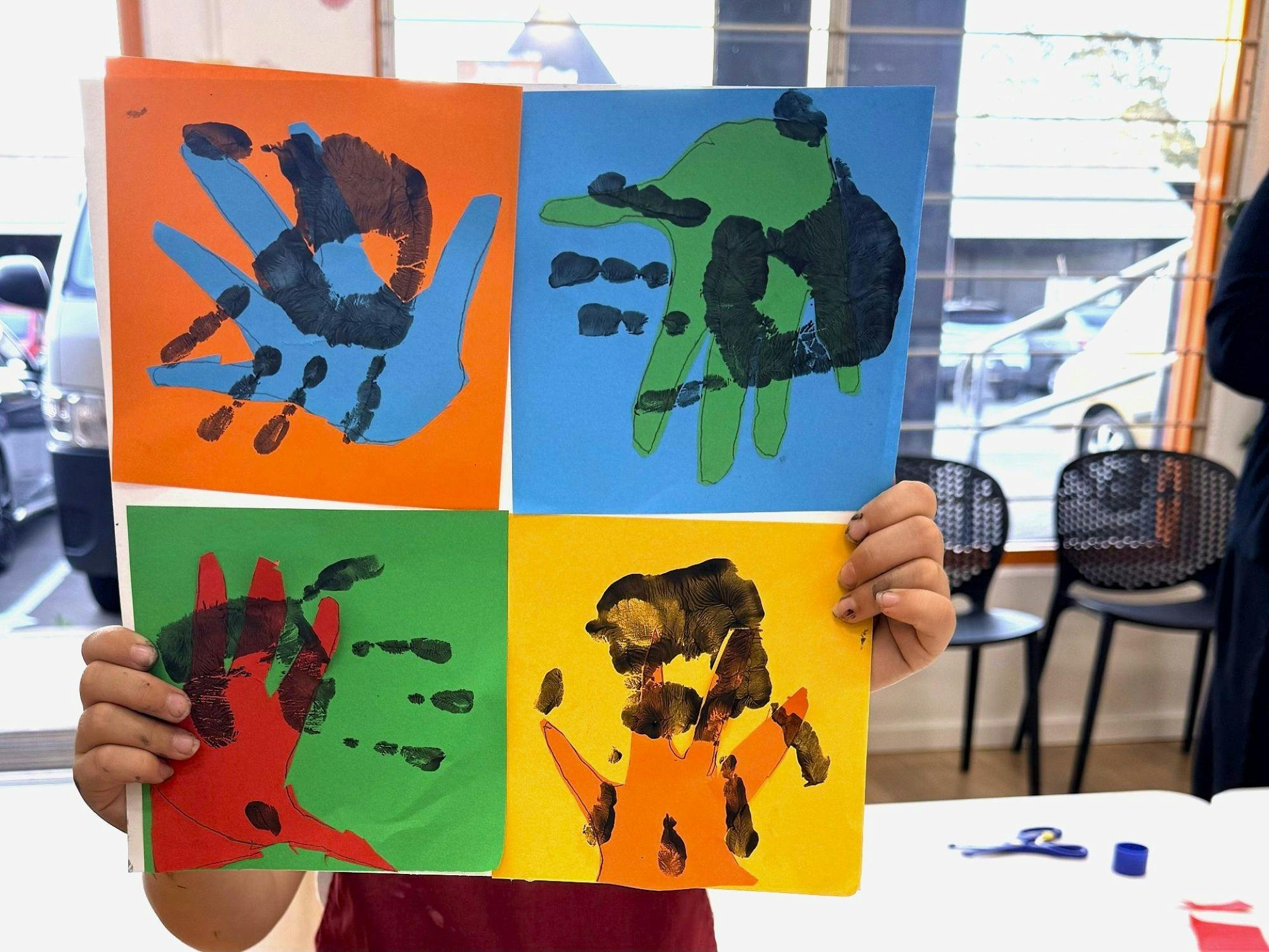 Child holding up a brightly coloured artwork featuring their hand-prints
