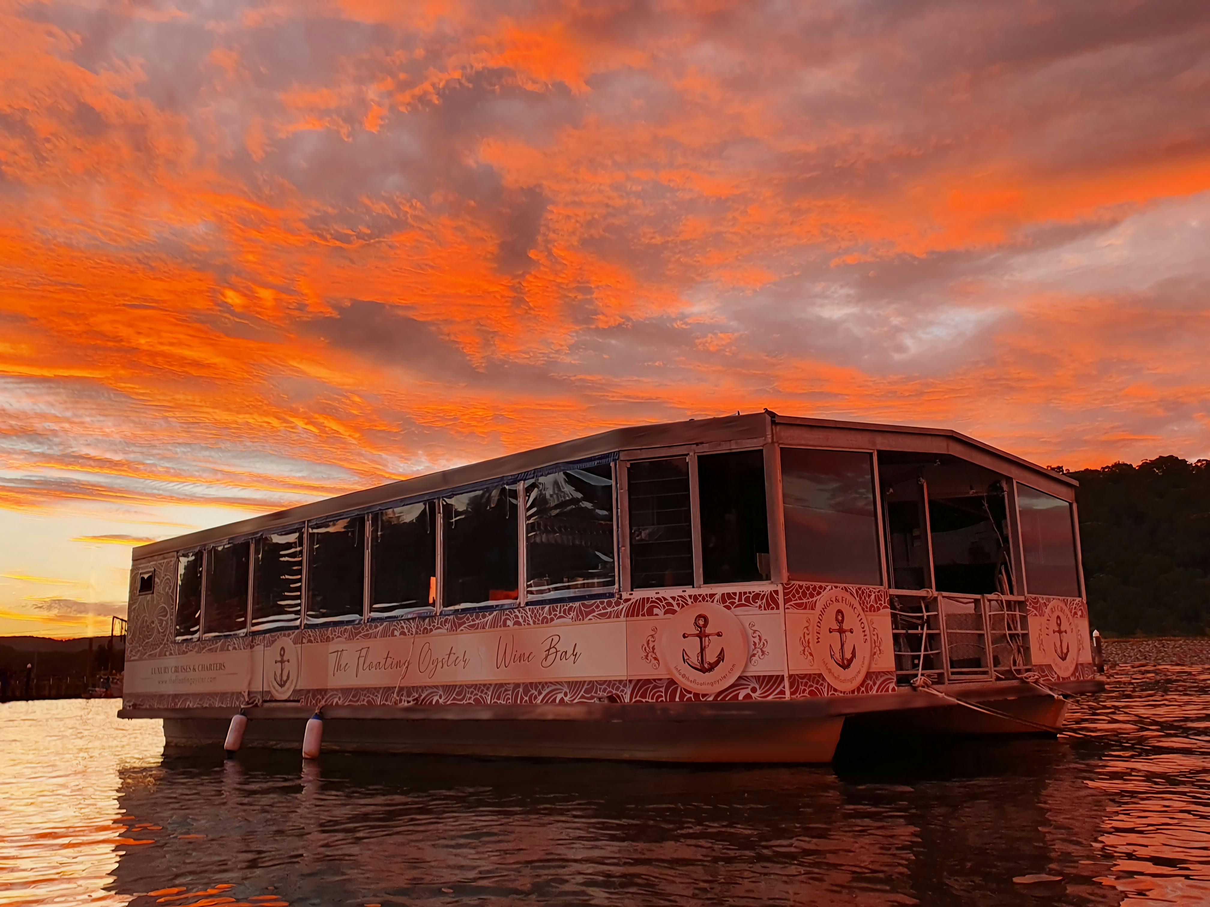 Beautiful orange sunset behind The Floating Oyster Wine Bar. Wide pontoon boat diagonally positioned