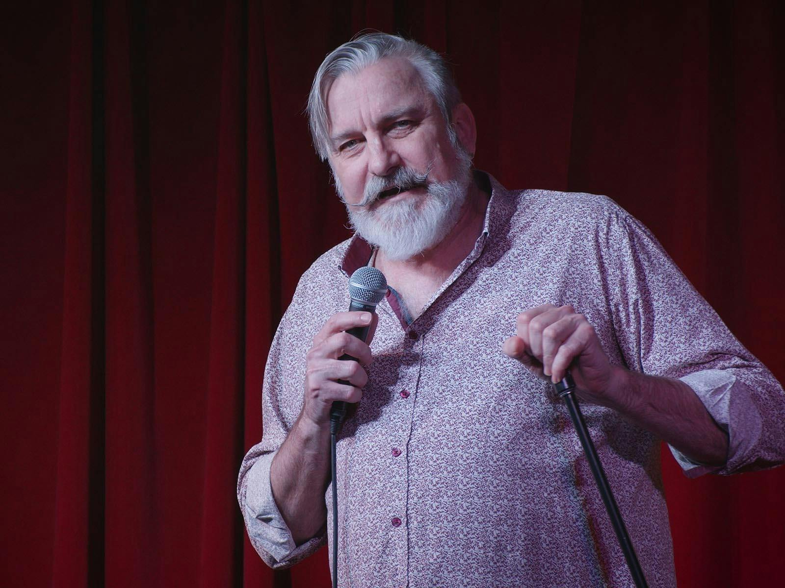 A white man in a beige shirt holding a mic