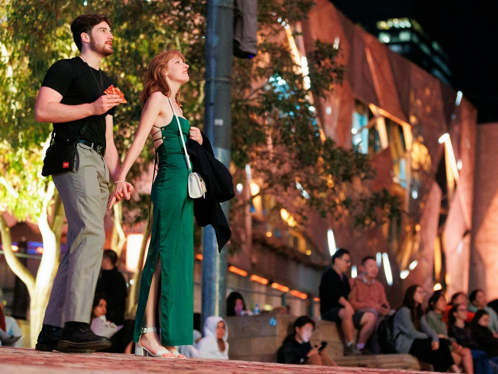 a couple hold hands at night in Fed Square