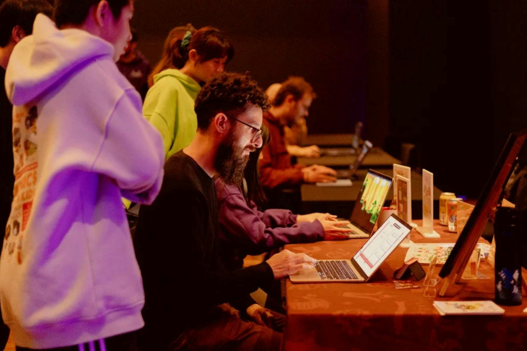 A man with a beard sits at a laptop playing a game