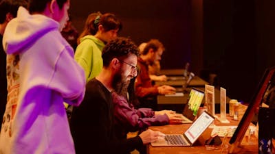 A man with a beard sits at a laptop playing a game