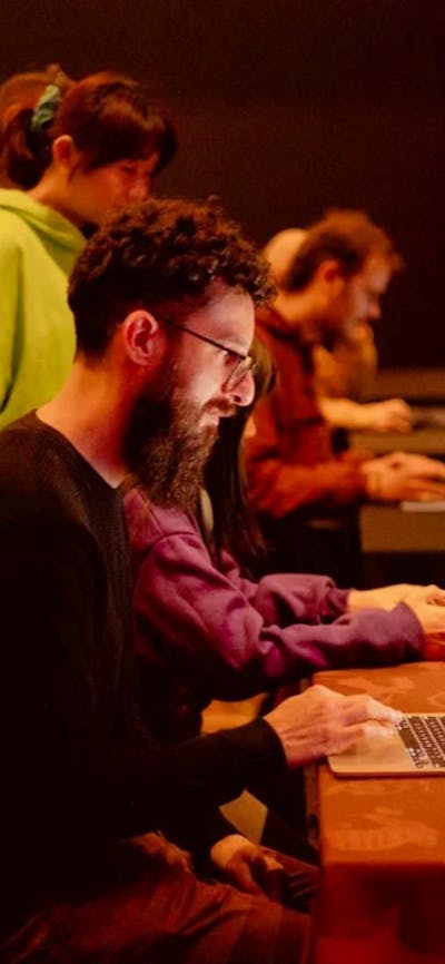 A man with a beard sits at a laptop playing a game