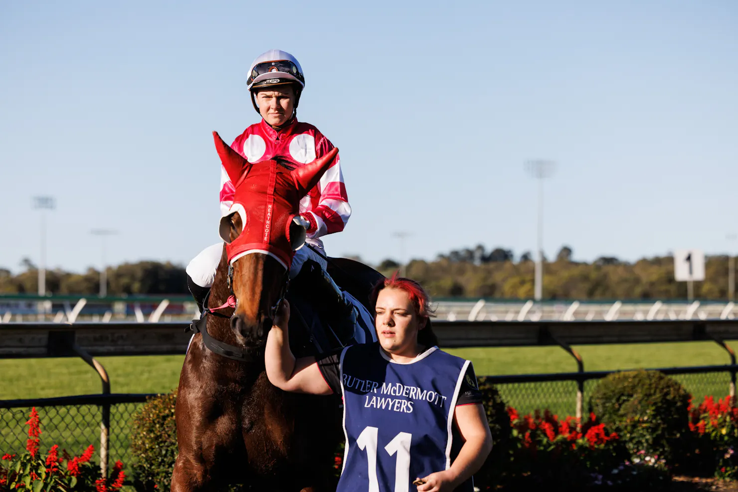 Jockey sitting on a Thoroughbred horse with a horse strapper guiding the horse in the mounting yard.