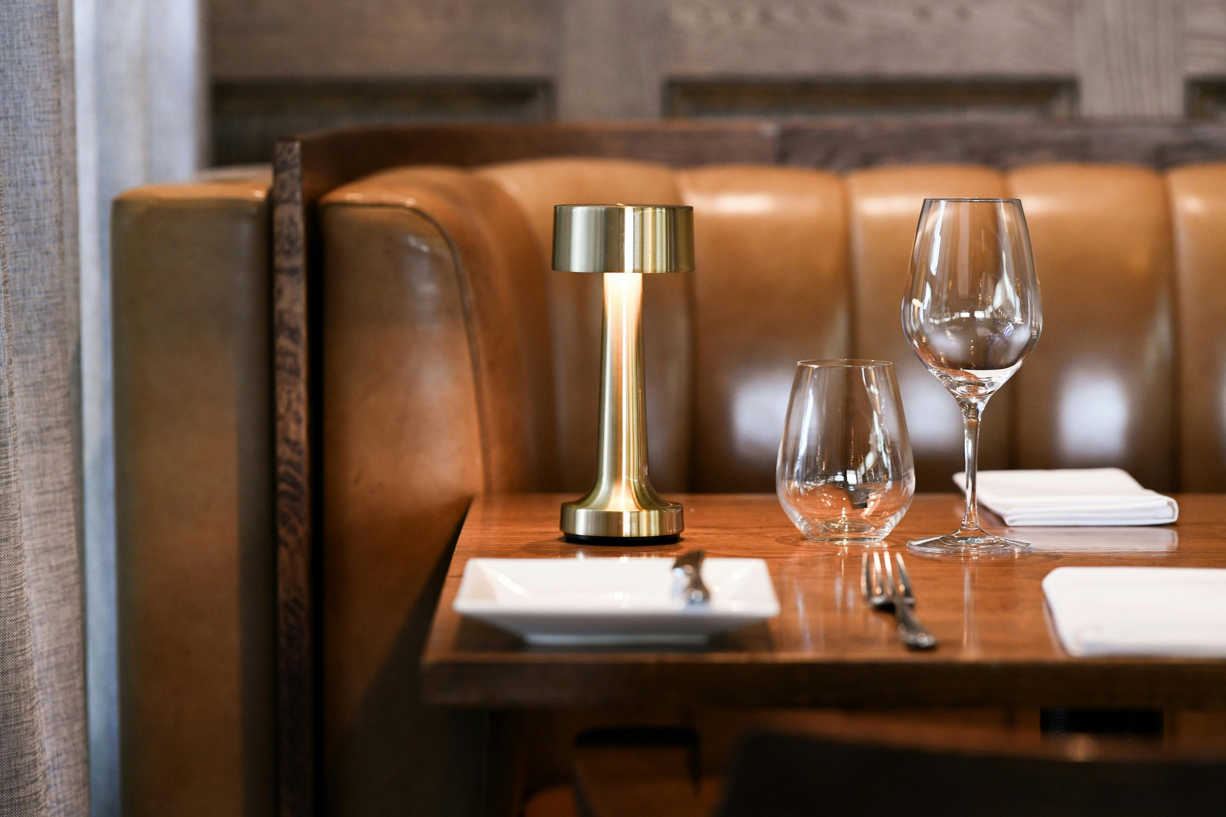 Elegant restaurant booth with leather seating, gold table lamp, and set glassware.