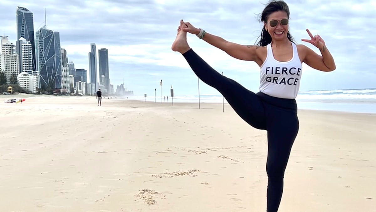 Director and Head Teacher, Rozlynn Hobbs yoga pose on the beach with Surfers skyline background.