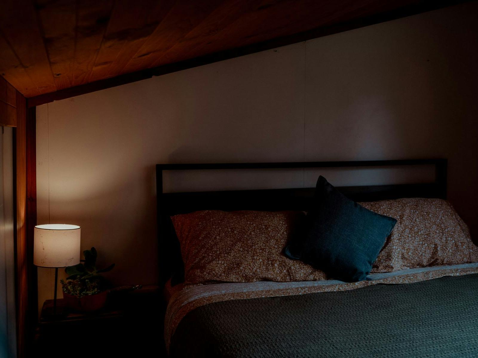 A cozy bedroom with sloped ceiling, warm lamp light, and earth-toned bedding.