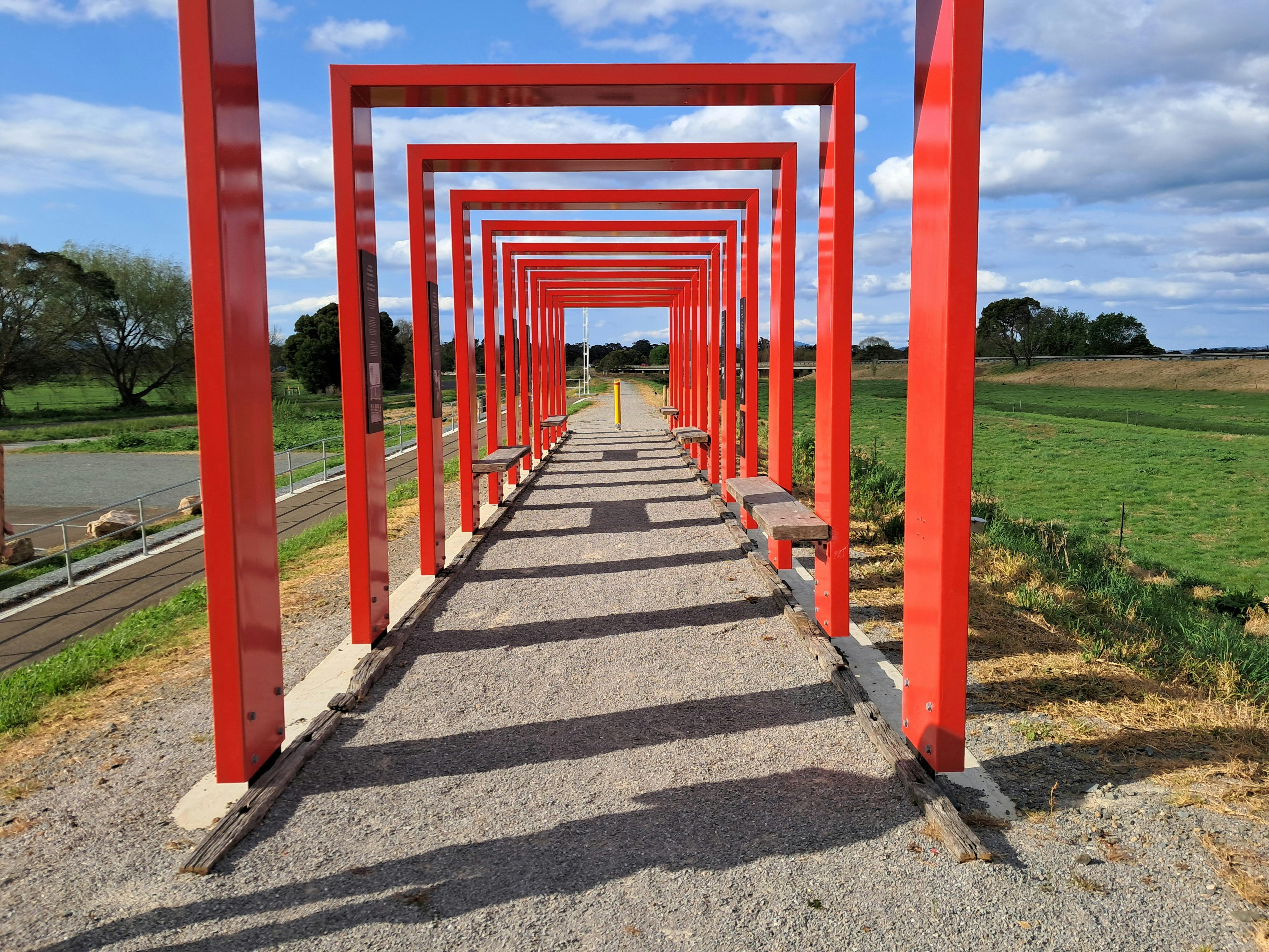 Geometrical red steel colonnade with walking trail leading to rail bridge