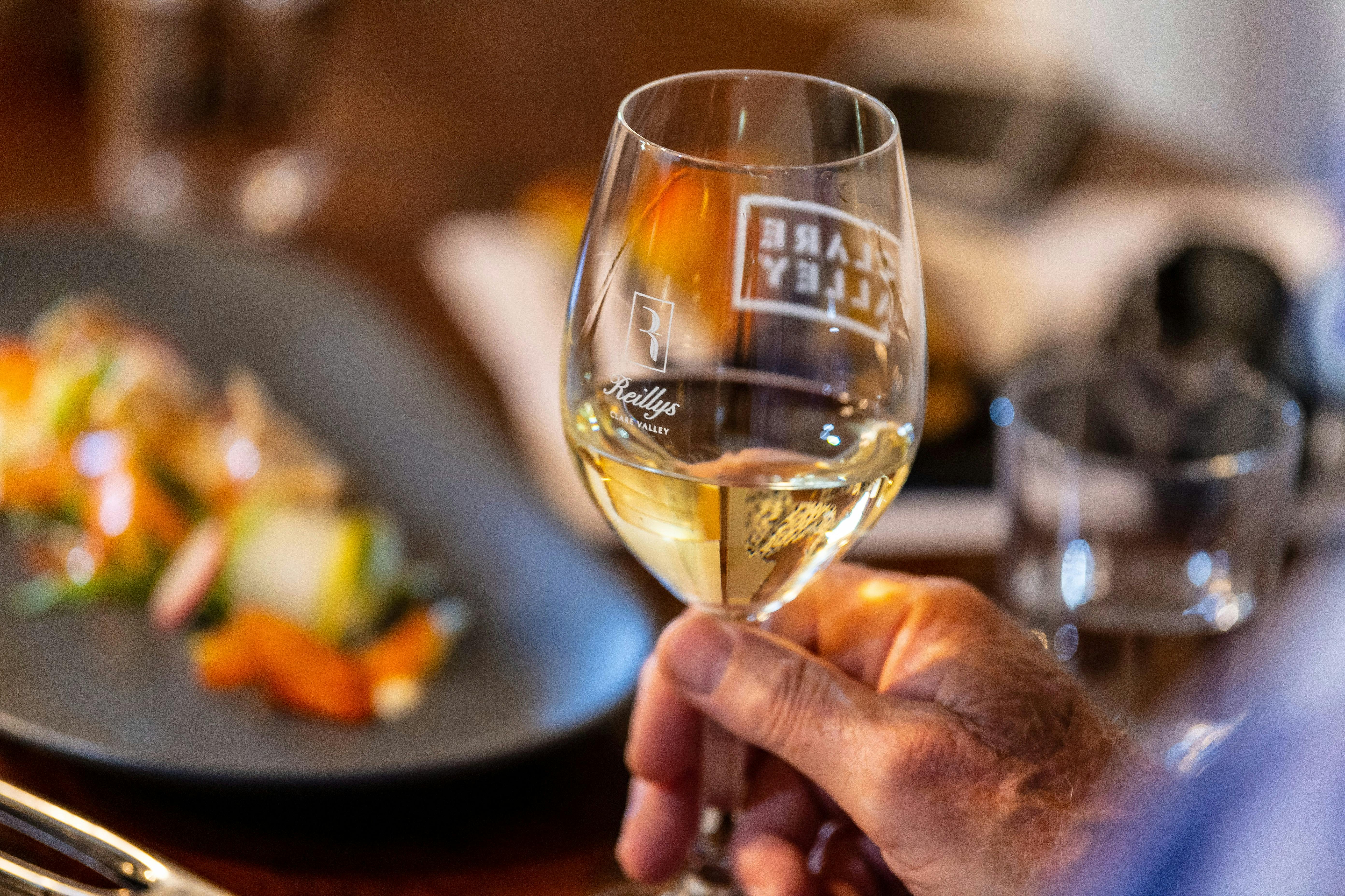 Holding a wine glass half-filled with white wine over a table with plates of food