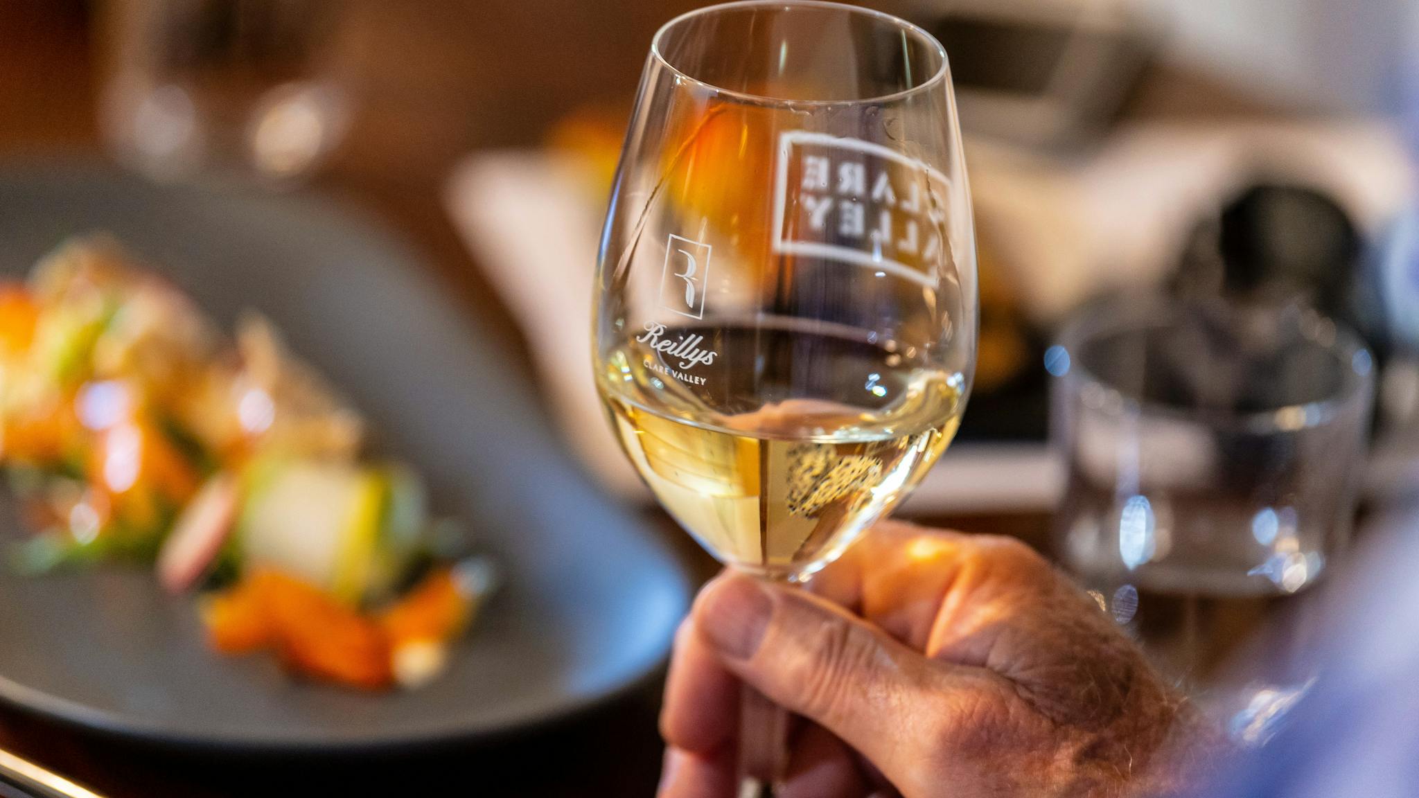 Holding a wine glass half-filled with white wine over a table with plates of food