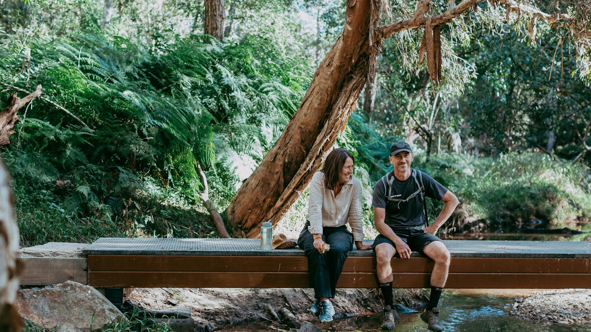 A happy couple sitting on a small bridge over a creek at Redlands Track Park, QLD.
